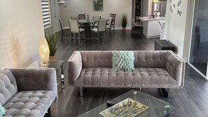 Una sala de estar moderna con un sofá seccional, una mesa de centro de vidrio y un comedor con una mesa y sillas.