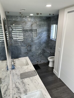 Une salle de bain moderne avec une douche à parois de verre, un grand miroir et un comptoir en marbre.