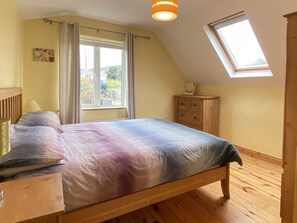 Een slaapkamer met een bed, een houten dressoir en een raam met gordijnen.