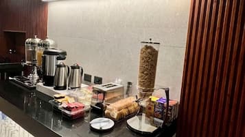 Un comptoir pour le petit-déjeuner équipé de machines à café, d’une cafetière, d’un distributeur de céréales et de divers produits pour le petit-déjeuner.