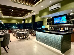 A modern bar area with a large TV screen, a bar counter, and seating for guests. - Hotel Myst (Monterrey)