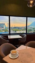 Una mesa con una taza de café, vista a un paisaje urbano a través de amplias ventanas y un diseño de interiores moderno.
