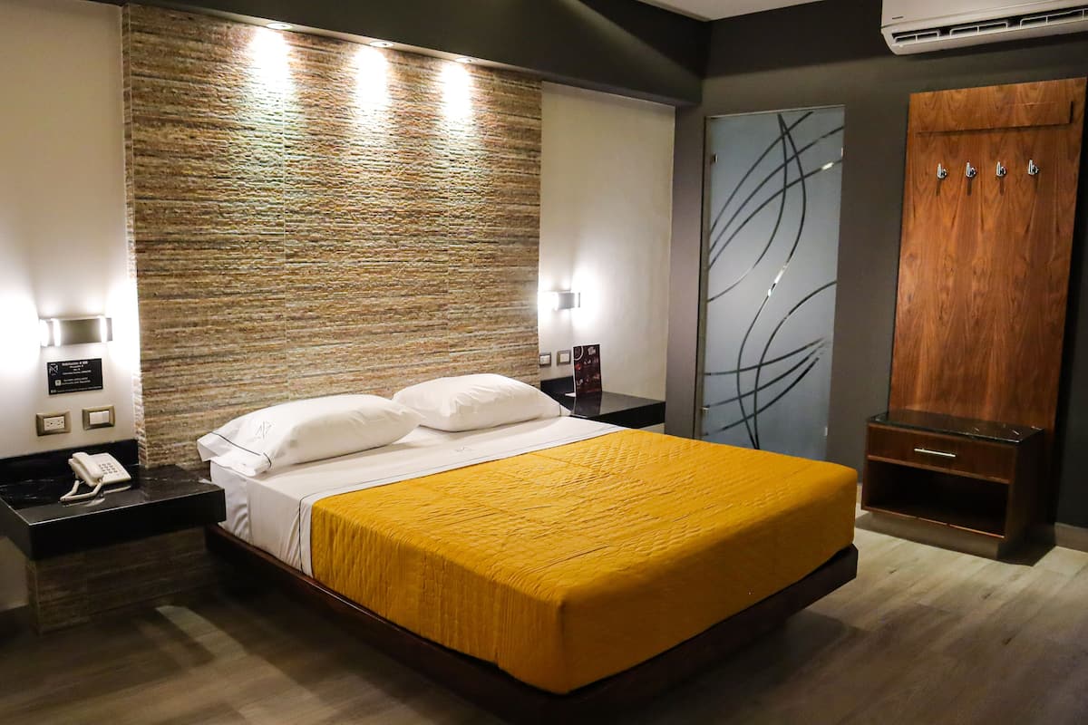 A modern hotel room with a large bed, a wooden headboard, a nightstand with a phone, and a wardrobe with a mirror.