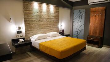 Una camera d'albergo moderna con un letto grande, una testiera in legno, un comodino con un telefono e un armadio con uno specchio.