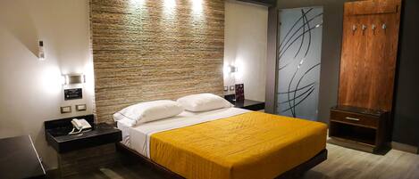 Habitación de hotel moderna con una cama grande, cabecera de madera, mesita de noche con teléfono y armario con espejo.