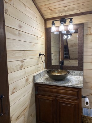 Ein Badezimmer mit Holzwandverkleidung, einem мраморном Waschbecken, einem großen Spiegel und einem Handtuchhalter.
