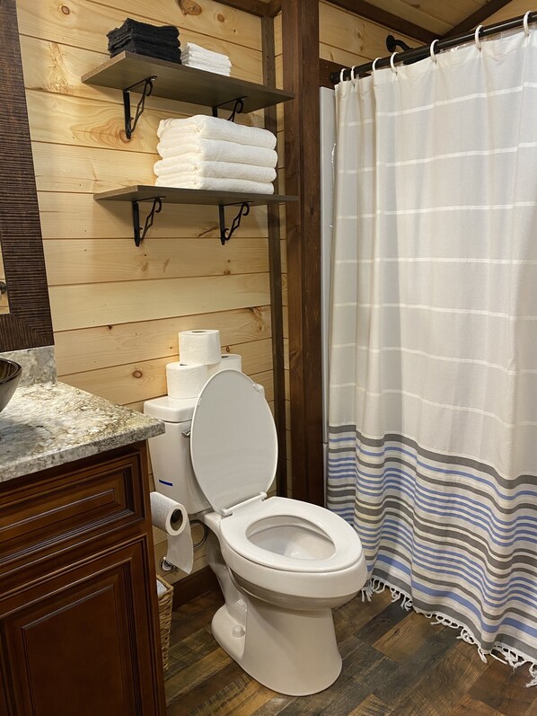 A bathroom with a wooden wall, a toilet, a shelf with towels, and a striped shower curtain.