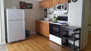 A compact kitchen with wooden cabinets, a white refrigerator, a microwave, a stove, and a small sink. - Three Islands Motel (Kawartha Lakes)