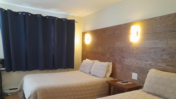 A hotel room with two beds, a wooden headboard, and a nightstand with a lamp. - Three Islands Motel (Kawartha Lakes)