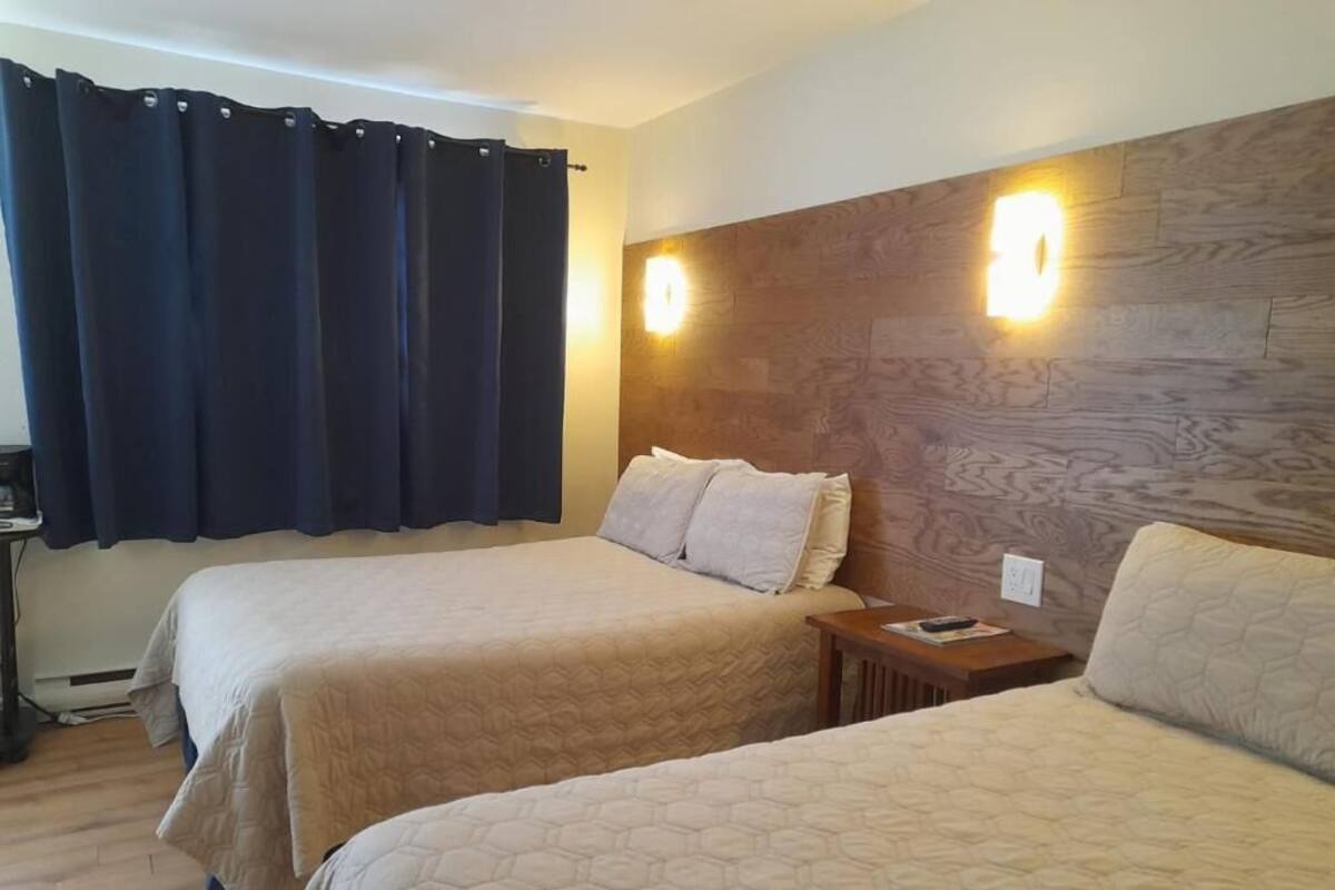 A hotel room with two beds, a wooden headboard, and a nightstand with a lamp.