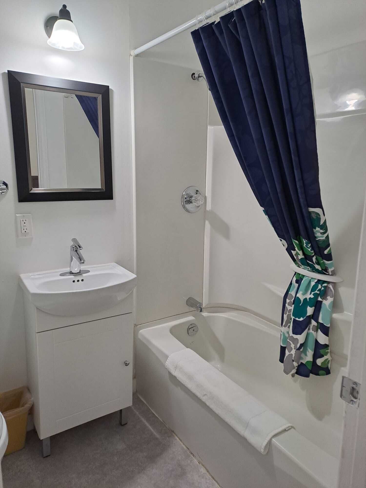 A bathroom with a white sink, a mirror, a shower curtain, and a bathtub.