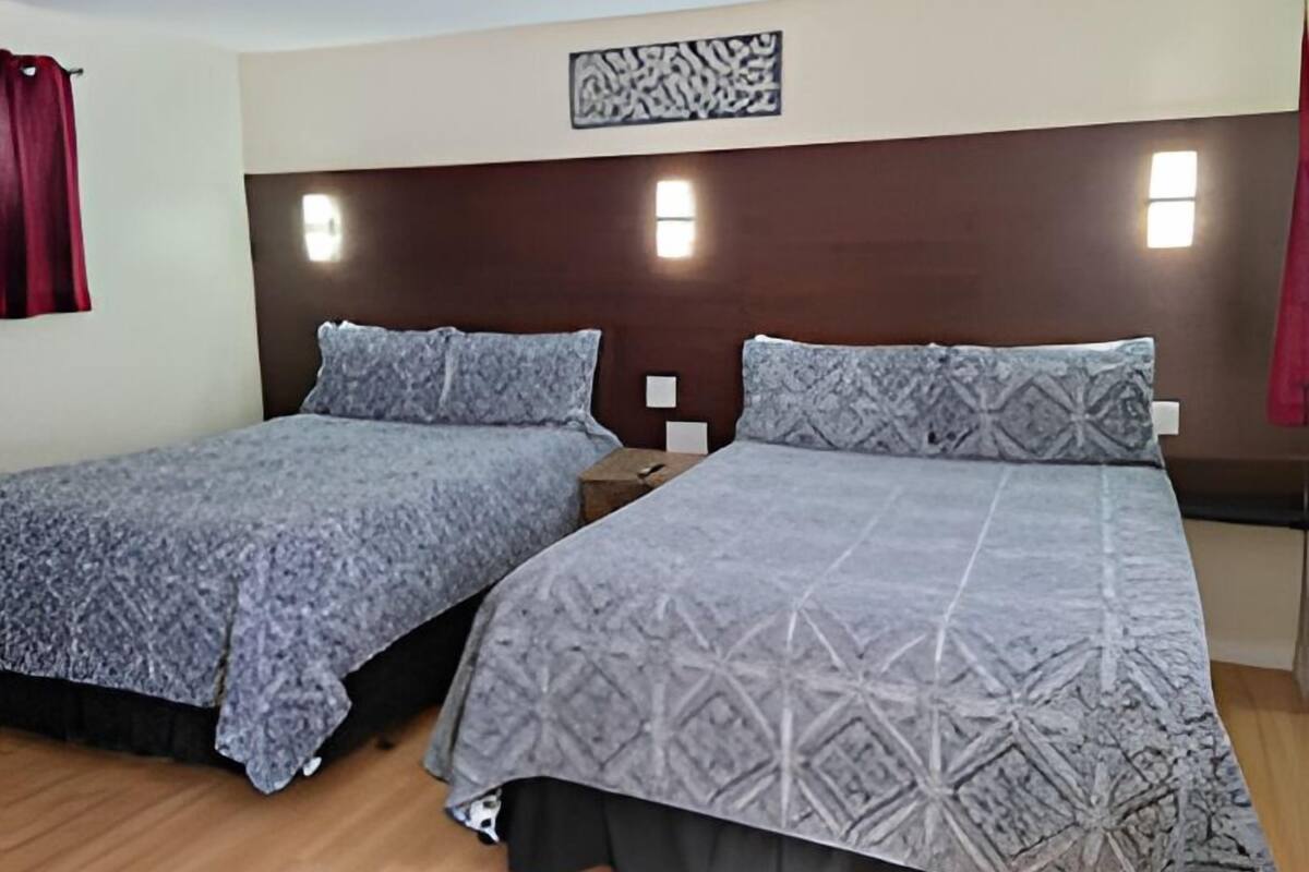 A room with two beds, each with a patterned bedspread and pillows, a wooden headboard, and a wall-mounted light fixture.
