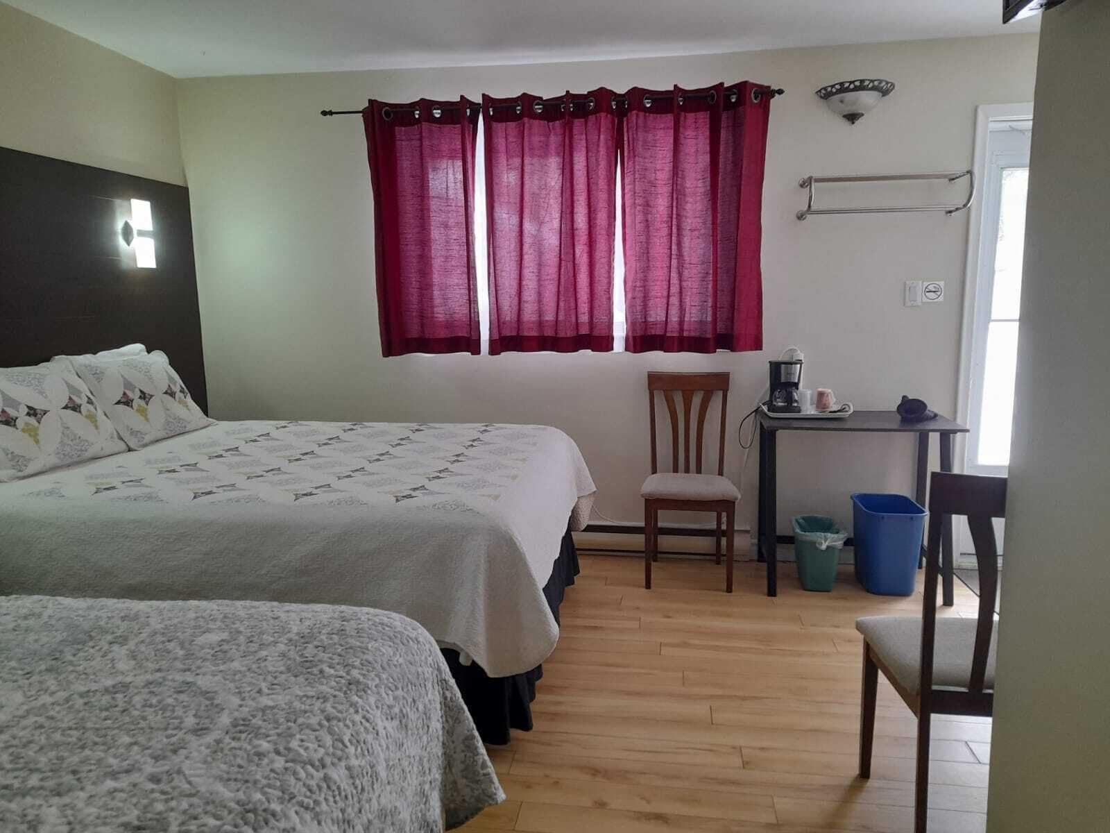 Un dormitorio con dos camas, un escritorio, una silla y una ventana con cortinas rojas.