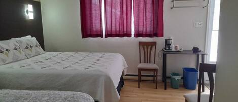 Un dormitorio con dos camas, un escritorio, una silla y una ventana con cortinas rojas.
