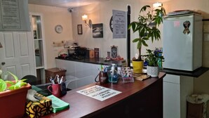 A reception area with a wooden counter, a refrigerator, a potted plant, and various items on the counter. - Three Islands Motel (Kawartha Lakes)