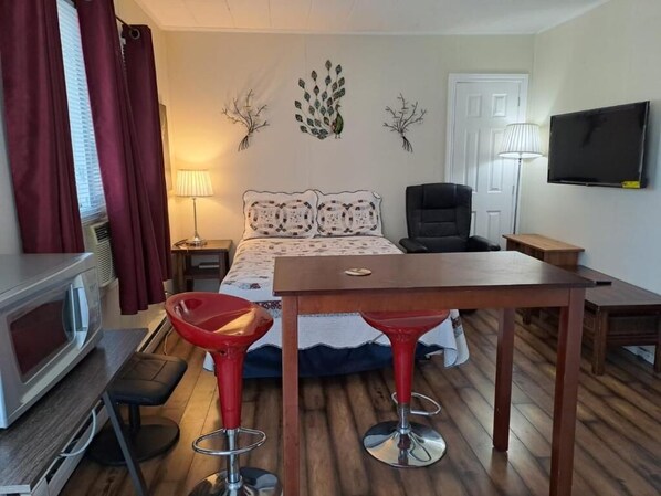 Una habitación de hotel con una cama, dos taburetes rojos, una mesa de madera, un televisor, una lámpara y un adorno de pared.
