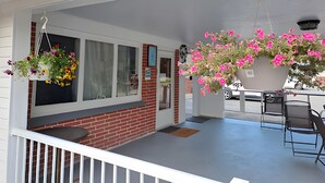 A covered porch with hanging flower baskets, a brick wall, and a table with chairs. - Three Islands Motel (Kawartha Lakes)