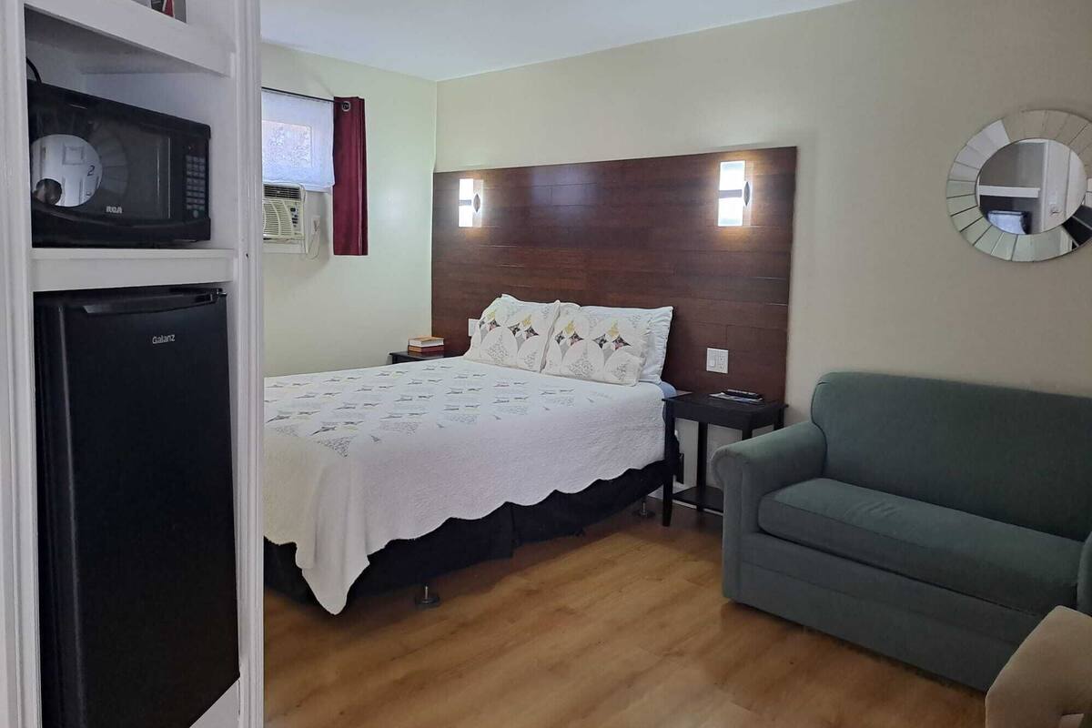 A bedroom with a bed, a nightstand, a green sofa, a microwave, and a refrigerator.