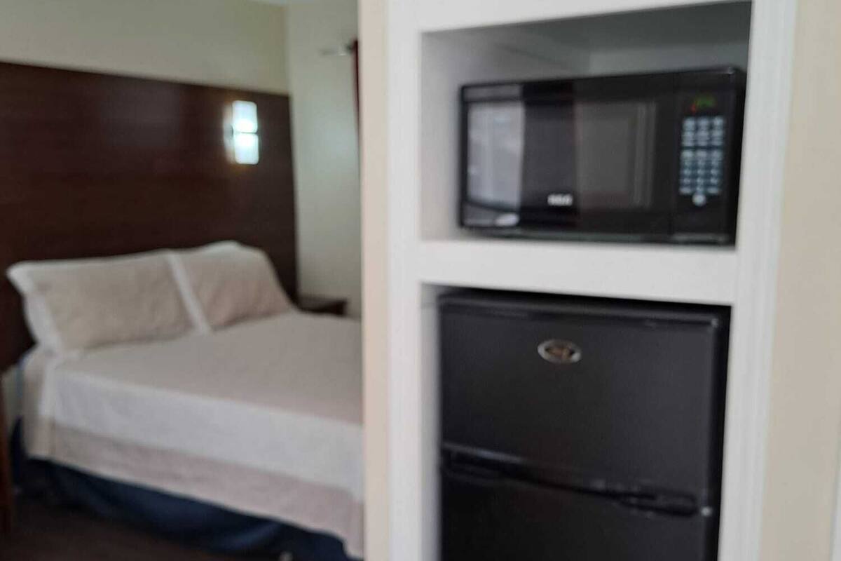 A hotel room with a bed, a microwave, and a refrigerator.