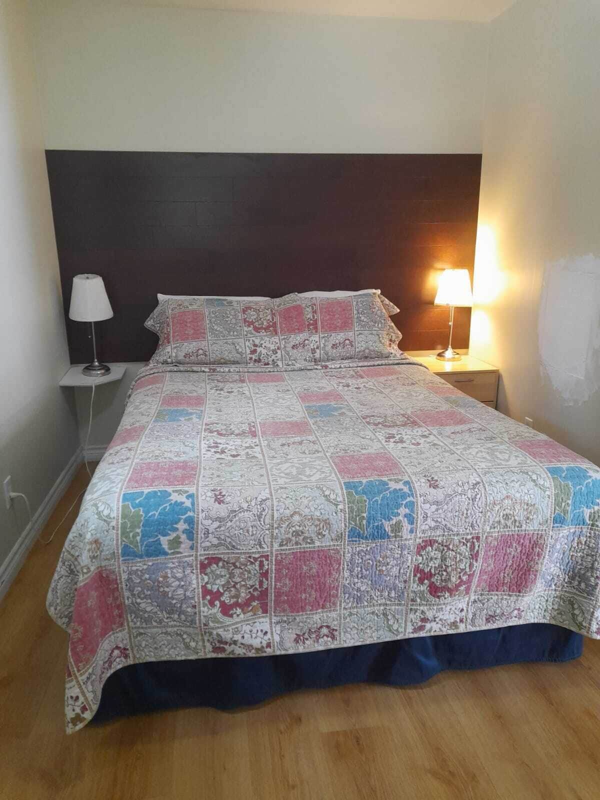 A bed with a quilt, two bedside lamps, and a dark headboard.