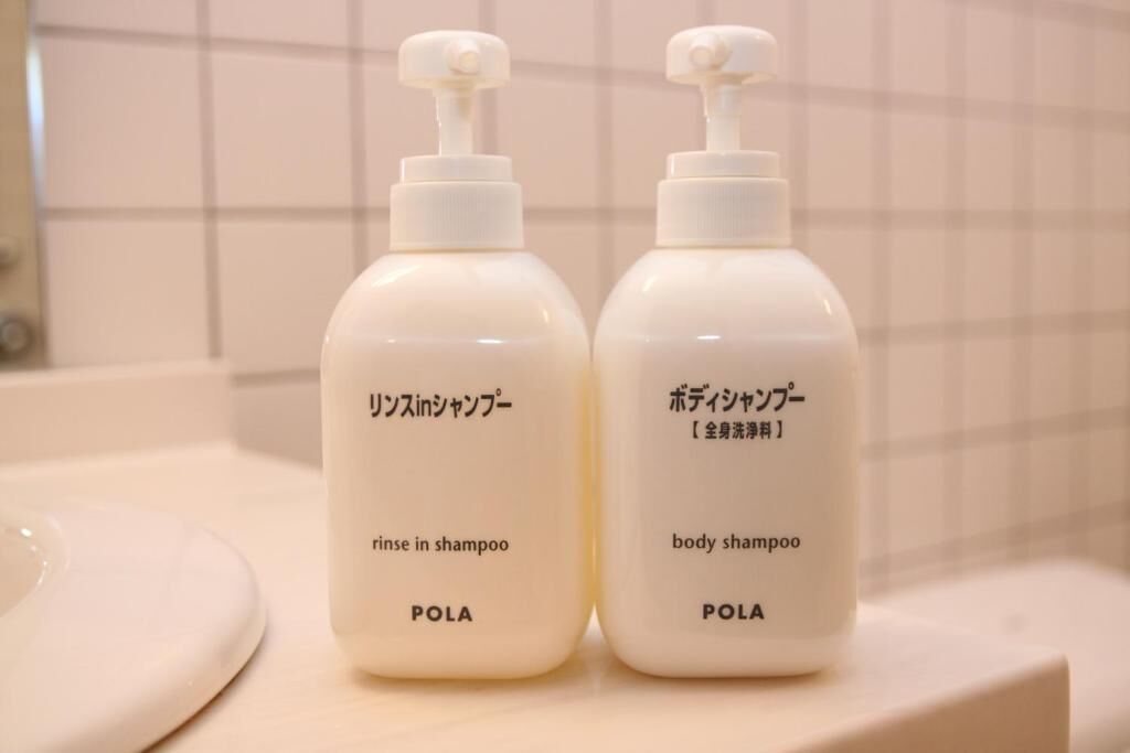 Two bottles of POLA body shampoo and rinse-in shampoo on a bathroom counter.