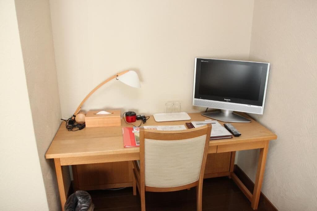 A wooden desk with a computer monitor, a lamp, a chair, and some office supplies.