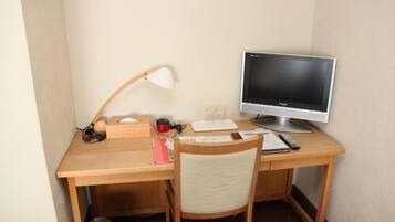 A wooden desk with a computer monitor, a lamp, a chair, and some office supplies.