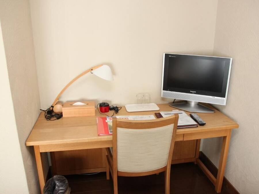 A wooden desk with a computer monitor, a lamp, a chair, and some office supplies.