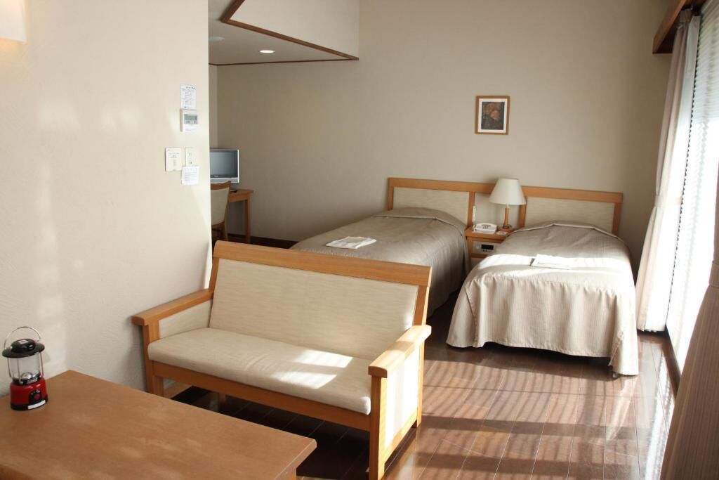 Habitación de hotel con sofá de madera, dos camas individuales, un escritorio con lámpara y televisión.