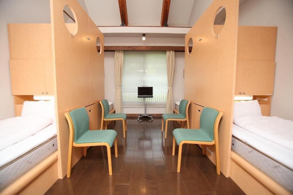 A hotel room with two beds, a TV, and a desk with chairs.