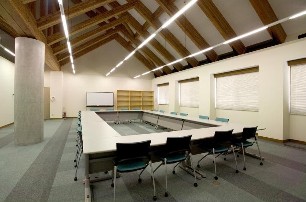 A conference room with a long table, chairs, a whiteboard, and shelves along the walls.