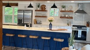 Een moderne keuken met een centraal eiland, barkrukken, een koelkast, een fornuis en een spoelbak.