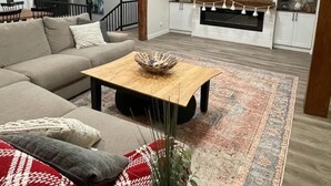 Een moderne woonkamer met een hoekbank, een houten salontafel en een grote flatscreen televisie aan de muur.