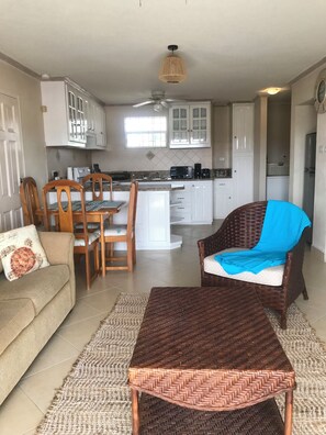 Ein Wohnzimmer mit einer Couch, zwei Holzstühlen, einem Korbtisch und einem Essbereich mit Tisch und Stühlen.