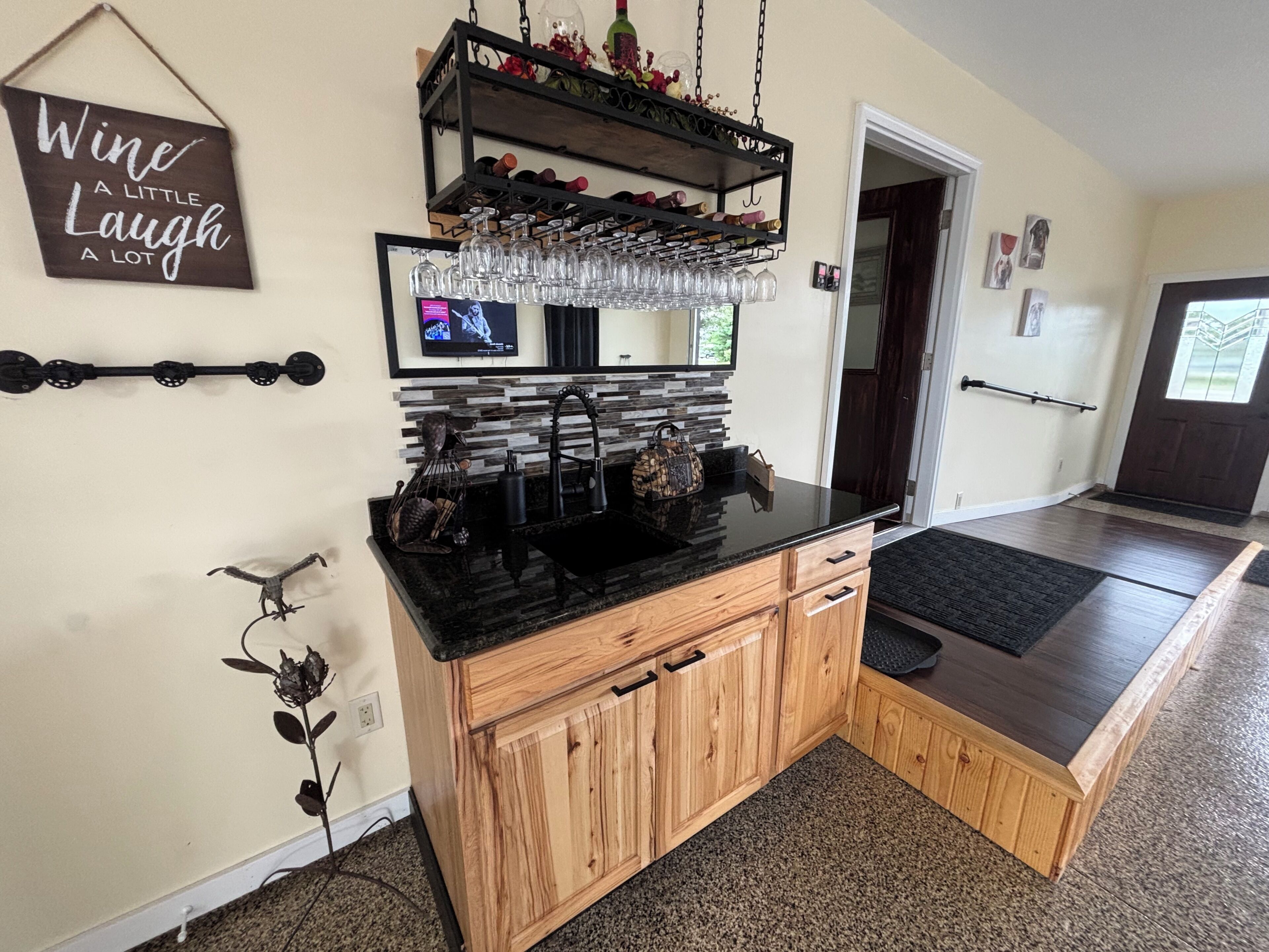 Une cuisine dotée d’un plan de travail noir, de meubles en bois, d’un meuble à vin et d’un téléviseur fixé au mur.