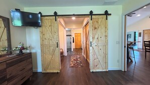 A hallway with wooden doors, a television mounted on the wall, and a rug on the floor. - Rusty’s Getaway is a rustic/modern handicap accessible, family friendly space.  (Findlay)
