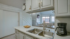 A kitchen with white cabinets, a stainless steel sink, a coffee maker, and a basket on the counter. - Condo within walking distance of the Chile Express (Angel Fire)
