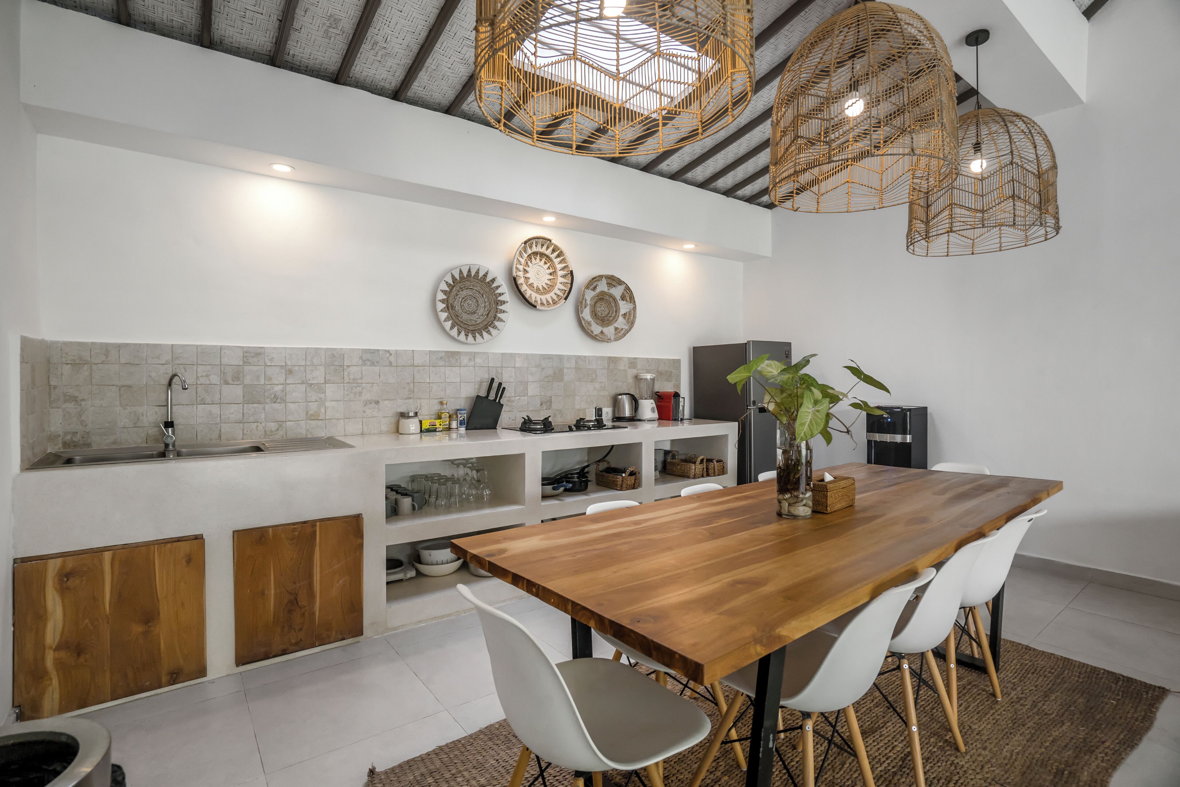 A modern kitchen with a wooden dining table, white chairs, and a hanging light fixture.
