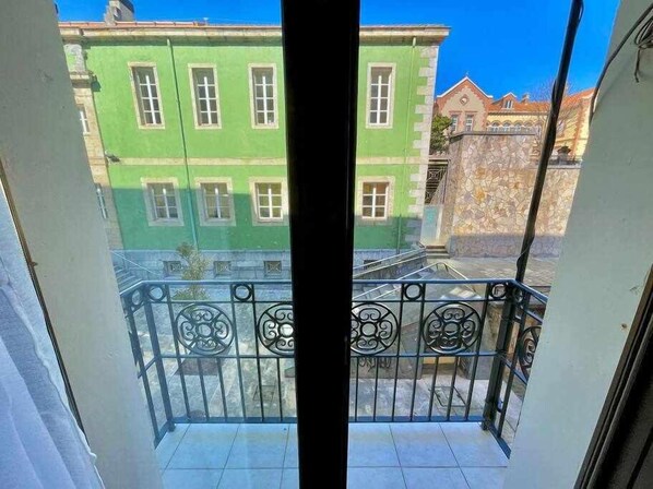 A balcony with a metal railing and a view of green buildings in the background.