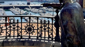 A statue overlooking a marina with boats and buildings in the background.