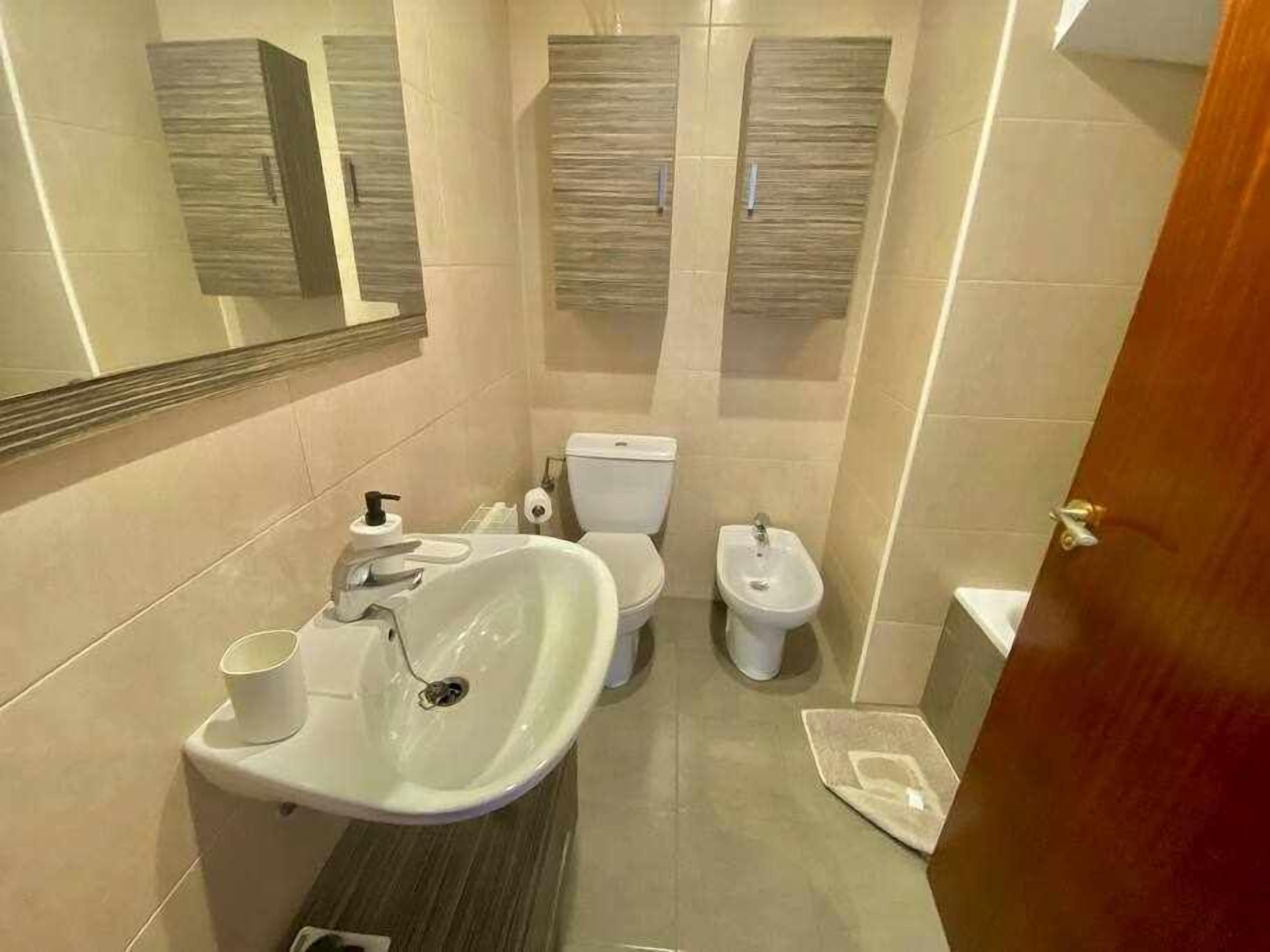 Et moderne badeværelse med vask, toilet, bidet og et spejl.