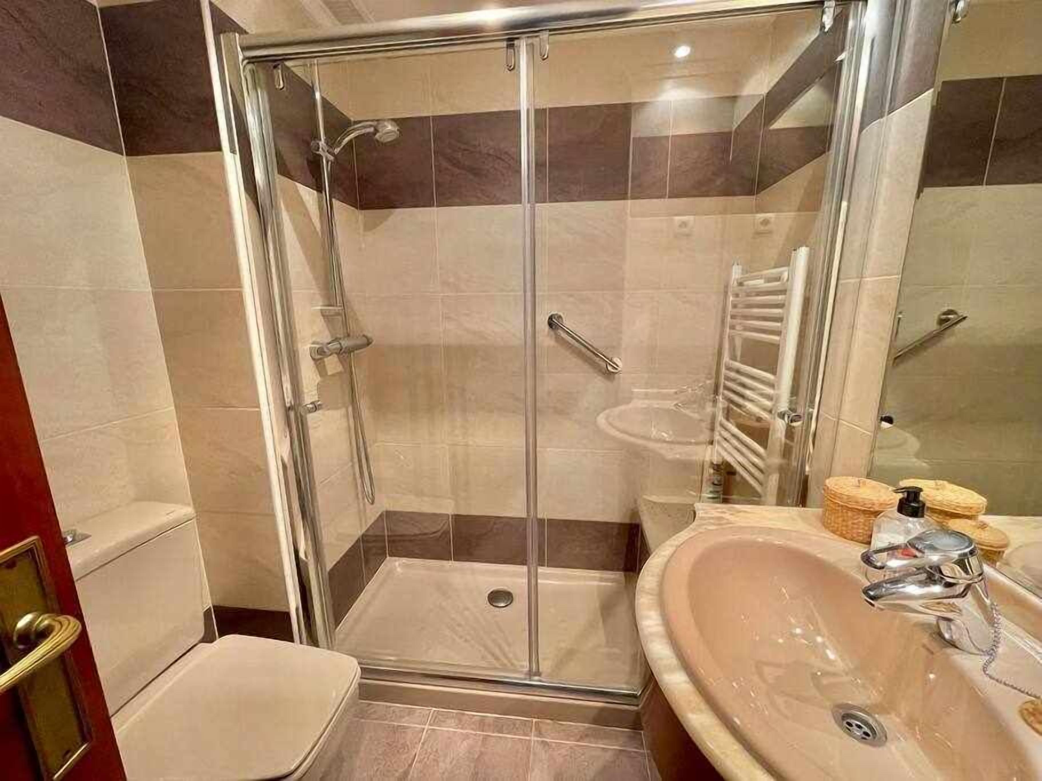 Un baño moderno con ducha envuelta en vidrio, tocador con lavamanos y un inodoro.