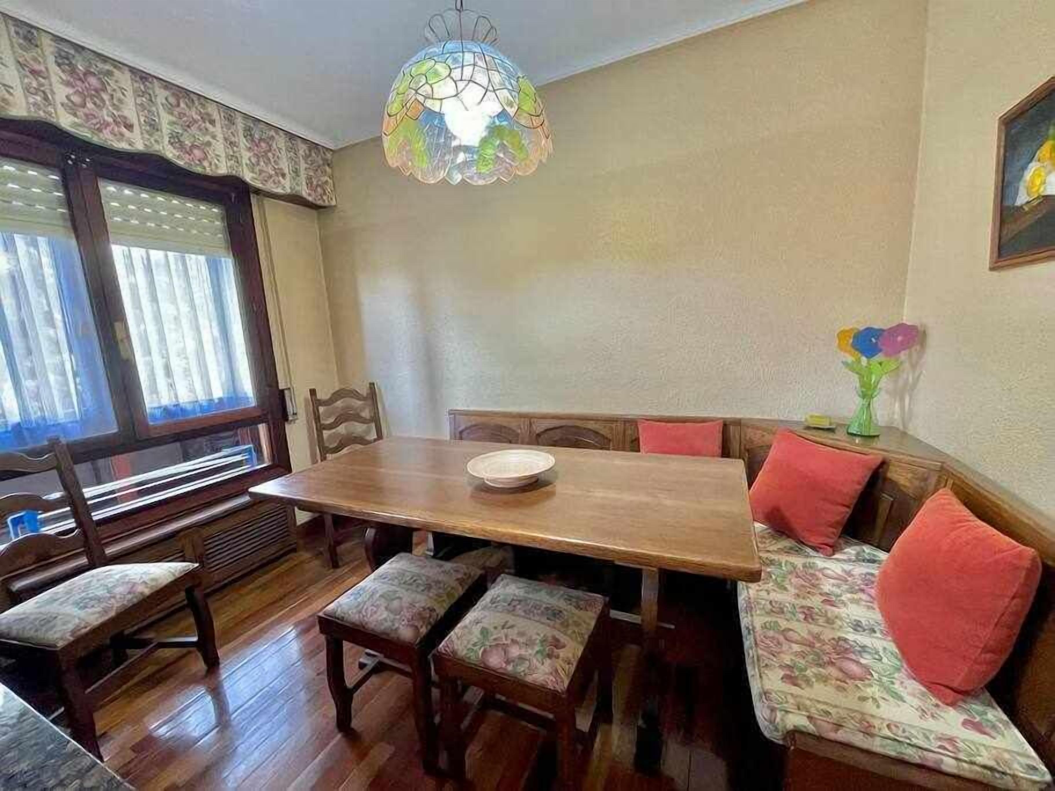 Un comedor con una mesa de madera, bancos acolchados y una lámpara de techo de vitral.