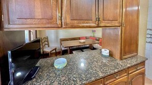 A kitchen with wooden cabinets, a granite countertop, a dining table with chairs, and a TV on the left. - Amatxo Maitia - Large movie apartment. (Bilbao)