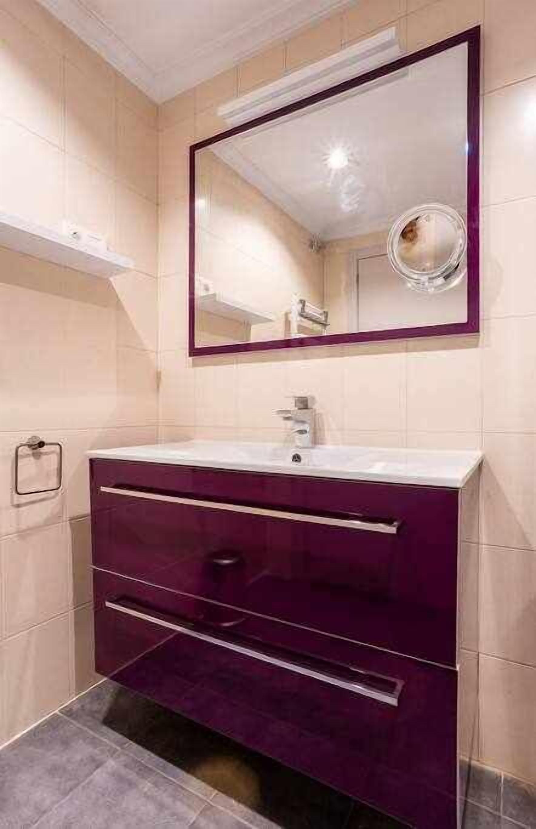 A bathroom with a white sink, purple vanity, and a large mirror above it.