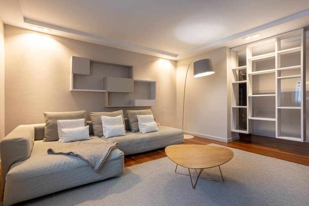 Ein modernes Wohnzimmer mit grauem Sofa, rundem Couchtisch und Einbauschränken.