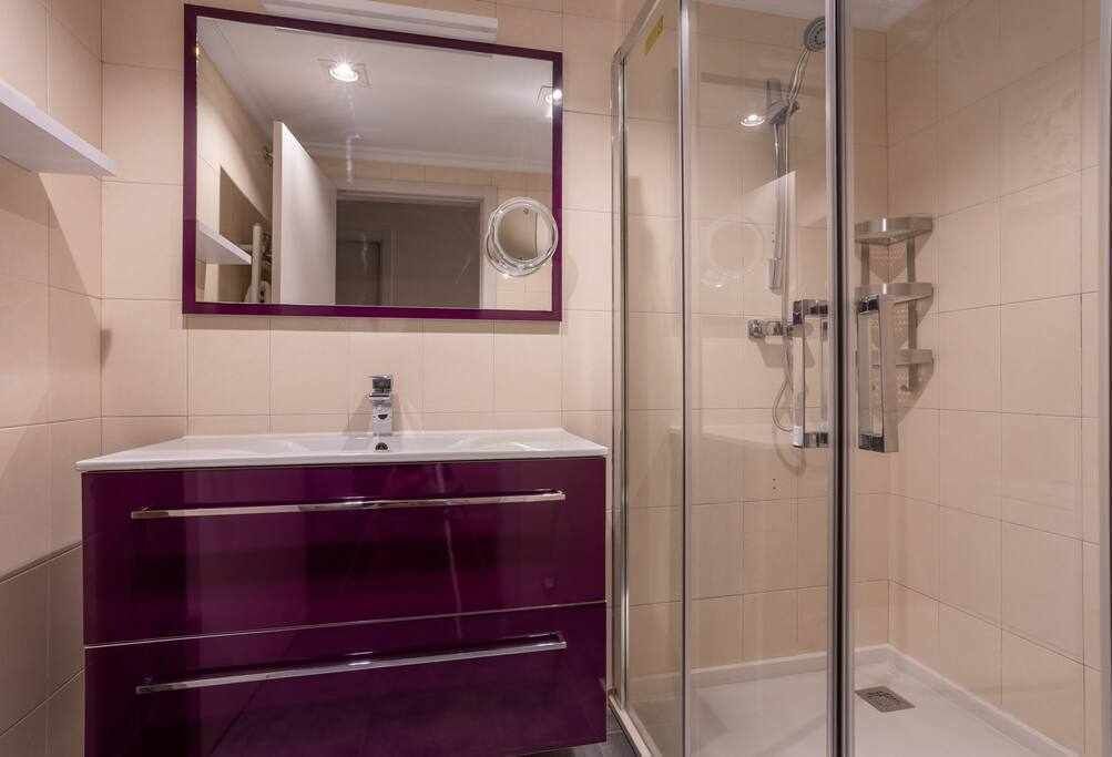 A bathroom with a glass-enclosed shower, a vanity with a mirror, and beige tiled walls.