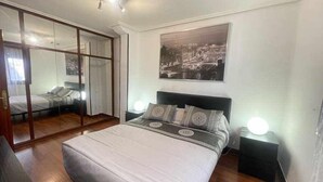 Une chambre avec un grand lit, une armoire avec un miroir et un tableau représentant un paysage urbain accroché au mur.