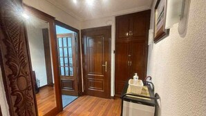 Un couloir doté d’un plancher en bois, une porte avec des panneaux de verre et une poubelle contenant une bouteille.