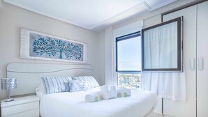 A bedroom with a bed, a nightstand, a window with curtains, and a wall-mounted artwork. - Old Port, Apartamento con Vistas al Puerto (Bermeo)